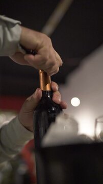 Close-up of man removing security seal from wine bottle at elegant dinner. Slow motion. Vertical. Argentina.