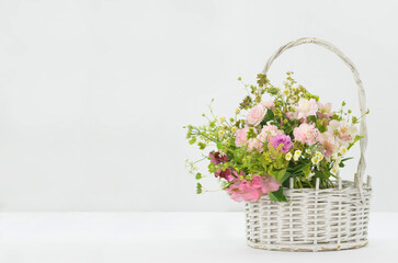 Fototapeta premium Bouquet of pink flowers in a basket on light background with empty space to fill with content, for example wishes.