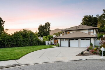 Fototapeta premium two-story house with a three-car garage, well-maintained lawn, and a scenic background at sunset
