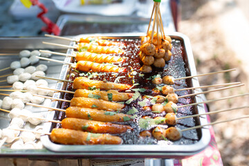 Fried meatballs and sausages on skewers soaked in dipping sauce are sold on trays.