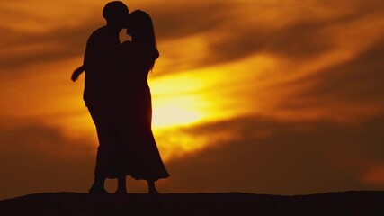 A couple is silhouetted against a sunset, with the man holding the woman's hand