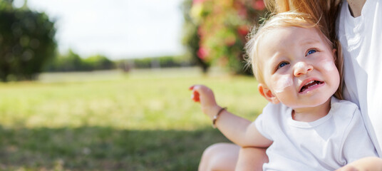 Female Toddler With Sunscreen On Face And Her Mother On Bright Green Grassy Garden. Concept Of Protecting Baby's Skin From Uv Rays. Concept Of Skin Cancer Prevention Or Aging. Child Taking Care. Baner