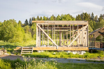 A small, unfinished house is surrounded by a lush green field