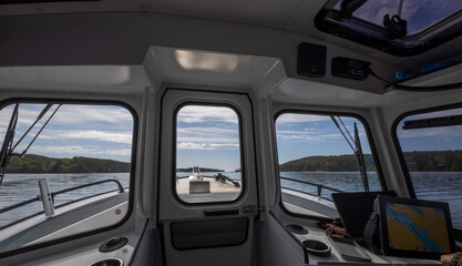 The interior of a boat with three windows offering a view of the calm water and a lush green...
