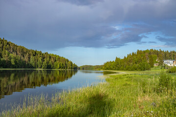 Obraz premium A picturesque scene of a calm lake surrounded by lush green forest, the water reflecting the sky and the trees in perfect harmony.