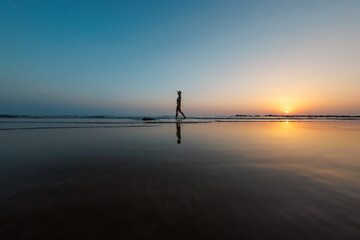 silhouette of a woman walking along the seashore. Spiritual Peace Meditation. A happy girl walks along the seashore against the backdrop of sunset.