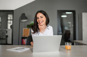 Beautiful young and cheerful businesswoman working on laptop in office