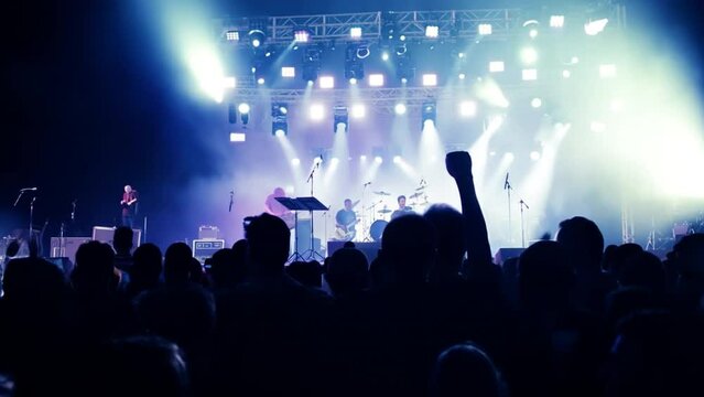 Rear back view of audience crowd people fans raising hands enjoying live music festival concert event rock band silhouettes performance sing on night club outdoor stage