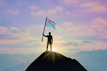 Waving flag of Fiji at the top of a mountain summit against sunset or sunrise. Fiji flag for...