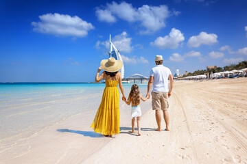 A tourist family on summer holiday time walks down a beautiful city beach in Dubai, United Arab...