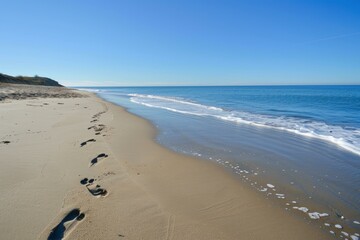 Tranquil and serene beach footprints on the untouched and deserted sandy shoreline with clear blue skies and calm ocean waves