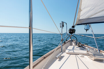 Obraz premium White yacht sailing on a sunny summer day. Top down view from the deck to the bow, mast and sails. Waves and water splashes. Clear blue sky. Gulf of Finland