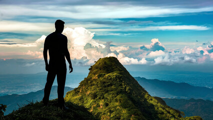 Fototapeta premium A silhouette of a man standing on a mountain peak, enjoying the sunrise and embracing the beauty of nature, symbolizing goals, hopes, and aspirations. 