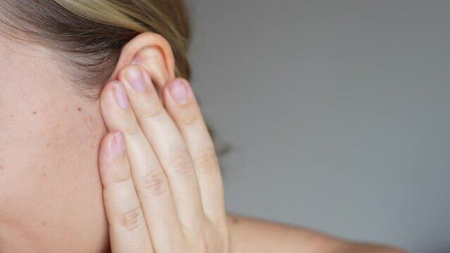 Cropped shot of a young caucasian woman holding her ears with her hand on a dark grey background. The girl suffering from severe ear pain and tinnitus, otitis