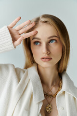 Blonde woman in white cardigan gazes thoughtfully.