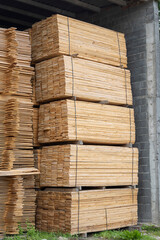 Large stacks of neatly arranged wooden boards are stacked outdoors on a bright, sunny day, likely for construction or woodworking purposes, against a natural backdrop.