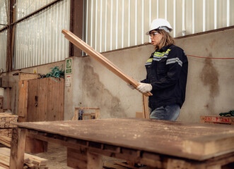 Confident female worker standing in lumber warehouse of hardwood furniture factory inspecting production machine. Serious female technician, engineer busy working with tool in woodwork manufacturing.