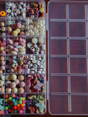 Kids Bead Set: A vertical, straight-from-above close-up shot captures beads in a plastic box, divided into sections based on their shapes, colors, and forms.