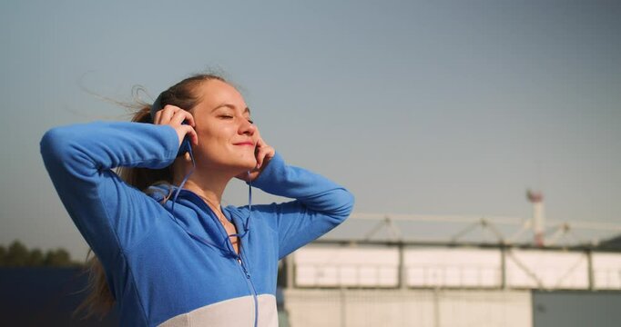 Sports in the urban rhythm of life. Middle aged sportswoman puts on headphones before morning workout. Favorite music as a motivator for your progress. Keeping your body in shape over 40.
