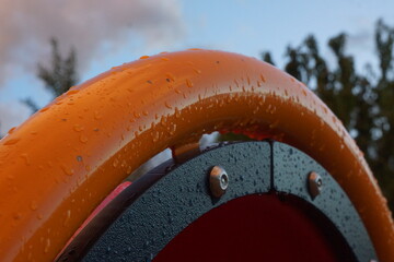 Macro of wet metal and plastic playground equipment, trees and light blue sky in background