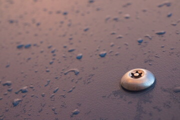 Macro of shiny metal bolt screwed in a plastic dark blue board with raindrops on it, well lit