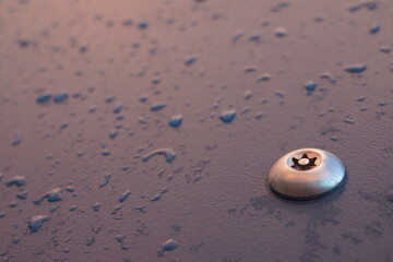 Macro of shiny metal bolt screwed in a plastic dark blue board with raindrops on it, well lit