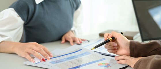 Cropped shot of businesswomen analyzing sales statistics document at office desk