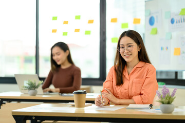 Portrait of smiling businesswoman sitting in an office with her colleagues in the background