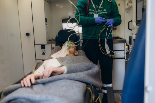 Top view of medic worker using valve mask bag on injured aged woman. Senior wounded female lying unconscious on hospital bed while doctor using oxygen bag