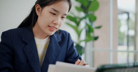Fototapeta premium Portrait of Asian businesswoman in suit use digital tablet for work and analyze documents in small coffee shop. Work from anywhere, Remote working