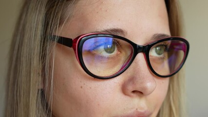Close up of young caucasian blonde woman putting on fashionable female glasses for working at a computer with a blue filter lenses on a light grey background. Anti blue light and rays. Eye protection