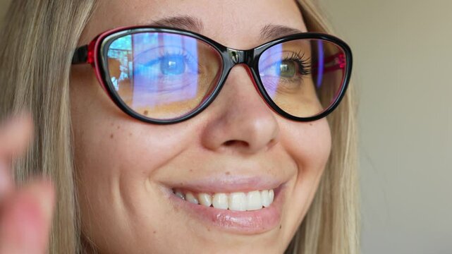 A squinting young blonde woman with poor eyesight putting on glasses for working at a computer with a blue filter lenses and becoming able to see well on a light grey background. Eye protection