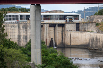 A large concrete dam with multiple gates and structures, surrounded by greenery, illustrating human engineering marvels and the serene environment it is part of.