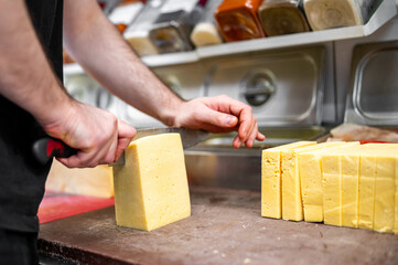 Hands cutting a block of cheese with a knife on a table