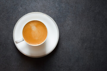 Top view of a morning espresso coffee or black coffee in a white glass cup on a black table background and copy space 2024. Beautiful coffee cup with foam of Americano on black background.