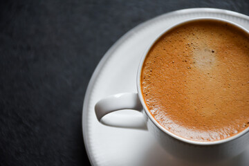 Close up of hot espresso coffee or Americano in a white glass cup on a black background 2024. Beautiful white cup of black coffee on the black table.