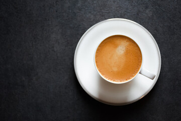 Top view of a morning espresso coffee or black coffee in a white glass cup on a black table background 2024. Beautiful of a coffee cup with foam of Americano on black background.