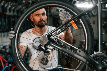 Spokes replacement. Repair man in bicycle shop, working in store