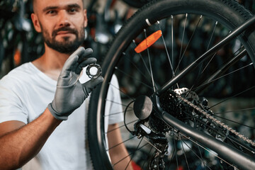 Holding circle shaped part near the wheel. Repair man in bicycle shop, working in store