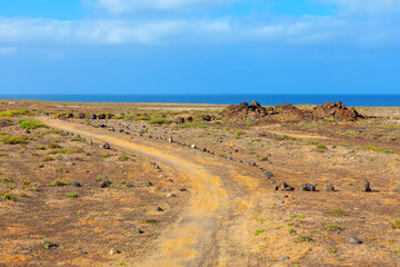 Coastal road at Canary Islands. Dirt road winds through a desert with a large body of water in the...