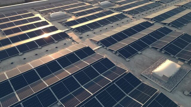 Moving backwards above solar panel power plant on roof during sunset, aerial view. Rooftop PV modules for renewable energy generation drone shot