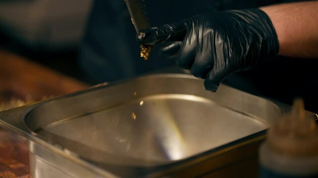 close-up in a restaurant in a rib bar in the central hall a chef in black gloves on a wooden board cuts Dijon mustard grinding for dressing pours into an iron bowl
