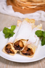 Homemade thin pancakes. The apples are cooked in a buttery caramel sauce with raisins and cinnamon and stuffed into a thin pancake. Garnish with powdered sugar and mint. Food in a rustic style.