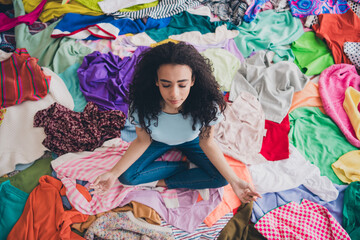 Above view full size photo of nice young girl sit meditate messy clutter clothes flat indoors