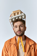 A young man wears an egg carton as a hat, with orange straps hanging down.