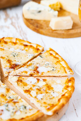 Pizza quattro formaggi on a wooden board .four cheese pizza and fresh ingredients for a four cheeses Italian pizza on a white wooden desk .