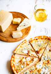 Pizza quattro formaggi on a wooden board .four cheese pizza and fresh ingredients for a four cheeses Italian pizza on a white wooden desk .