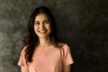 Radiating happiness, a young white woman smiles brightly, her expression full of warmth and optimism. A multiracial woman stands against a grey background on the right, providing space for copy.