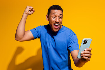 Photo portrait of attractive young man hold device winning dressed stylish blue clothes isolated on yellow color background