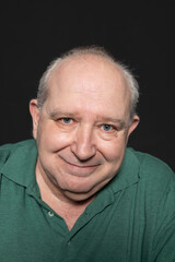 Portrait of a 60-year-old man with white hair and blue eyes looking at smiling camera on black background. Concept of aging